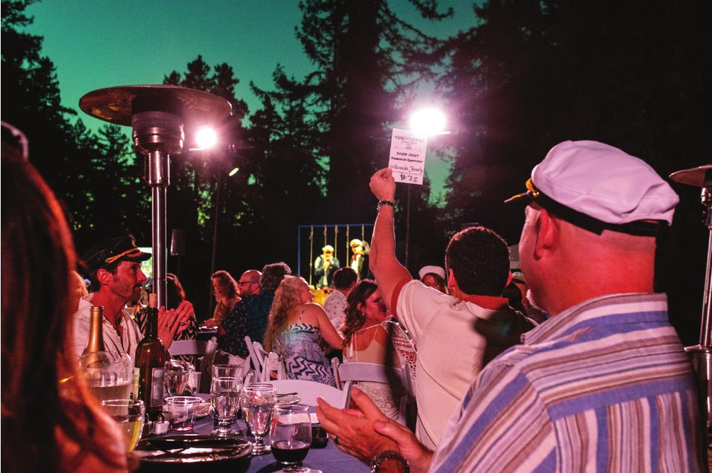 A bidder in a captain’s hat raising a paddle at the gala auction among the redwoods